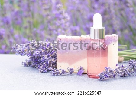 Lavender beauty products - pink dropper bottle with cosmetic oil and natural handmade soap bars against lavender flowers field as background. Herbal cosmetics, mockup