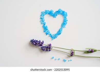 Lavender Flowers And Bath Salt. Blue Heart Of Lavender Bath Salt. Flat Lay Bath Salt, Spa Products And Lavender Flowers On White Background. Skin Care, Beauty Treatment Concept. Copy Space. 