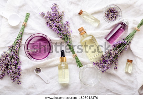 Lavender oils serum and lavender flowers on white\
fabric. Skincare cosmetics products. Set natural spa beauty\
products. Lavender essential oil, serum, body butter, massage oil,\
liquid. Flat lay
