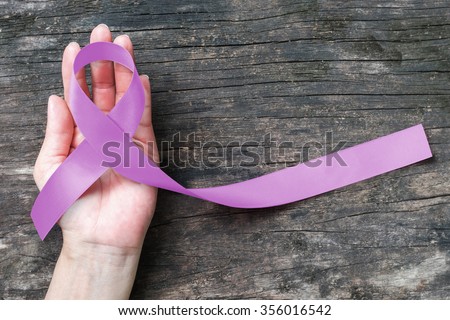 Lavender purple awareness ribbon on people's helping hand support with aged wood for world cancer day and National cancer survivor month to support patient with all kinds of tumor illness