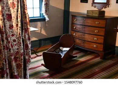 A Lavish Room For A Baby With A Traditional Colonial Crib. An Antique Wardrobe And Curtains With A Red Flower Design.