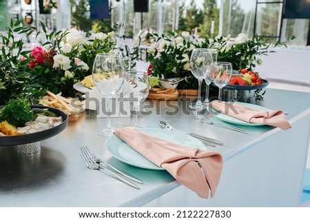 Lavishly decorated with roses banquet table outdoors. Plates with napkins, empty glasses and appetizers