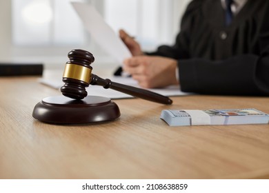 Law, auctioning, corruption, bankruptcy, bail, bribery or fines. Close up of judge gavel standing on sound block and bundle of dollars on table against background of judge or auctioneer with documents