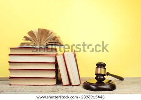 Law concept - Open law book, Judge's gavel, scales, Themis statue on table in a courtroom or law enforcement office. Wooden table, yellow background.