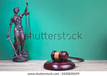 Law concept - Open law book, Judge's gavel, scales, Themis statue on table in a courtroom or law enforcement office. Wooden table, green background.