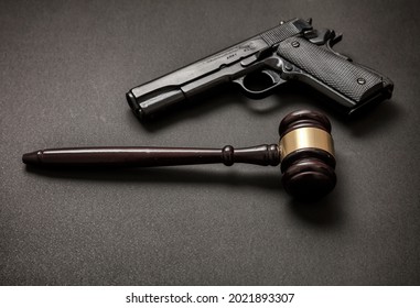 Law, crime, punishment concept. Judge gavel and a 9mm pistol on black background. Illegal weapon carry and use concept