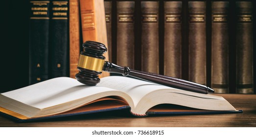 Law gavel on an open book, wooden desk, law books background