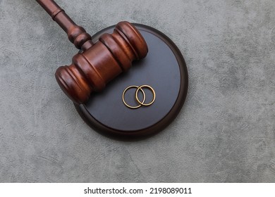 Law theme. Judge gavel wedding rings on concrete stone grey background. Divorce proceedings. Mallet of judge deciding on marriage divorce, marital agreement, legalities of divorce