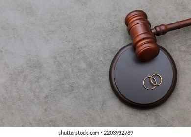 Law theme. Judge gavel wedding rings on concrete stone grey background. Divorce proceedings. Mallet of judge deciding on marriage divorce, marital agreement, legalities of divorce