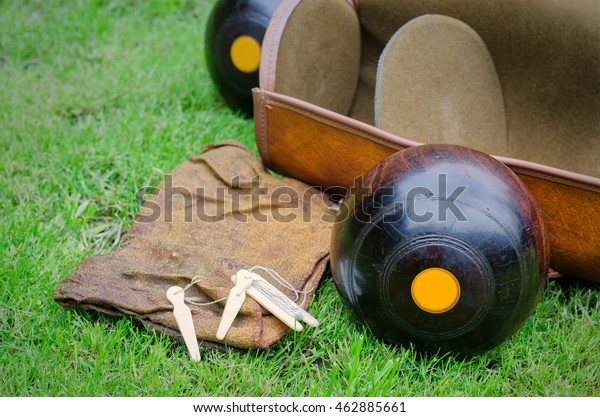 Lawn Bowls. Two wooden\
bowling balls on freshly cut grass with measuring device, leather\
bag and cloth. 