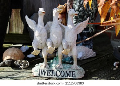 A lawn ornament of three white geese with their wings wrapped around each other representing friendship. The base says WELCOME.
