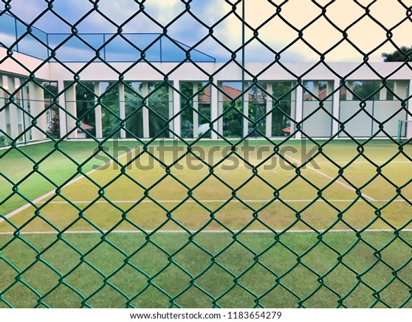 Lawn\
tennis court behind the grid chain link\
fence.