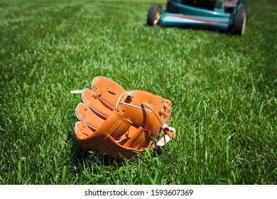 Lawnmower In Backyard About To Run Over A Baseball Glove Laying In The Grass