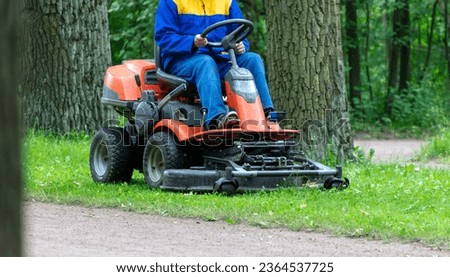 A lawnmower mows the grass in the park.