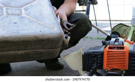 the lawnmower pours gasoline from a metal can into the mower container through a plastic funnel, refueling the lawnmower with fuel, pouring gasoline into the mower by a person - Powered by Shutterstock