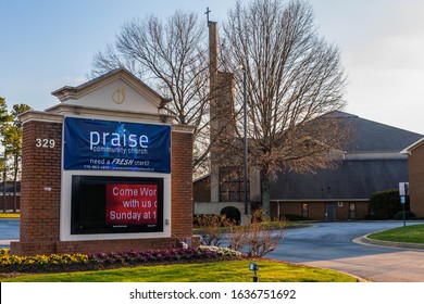 Lawrenceville, GA / USA - January 30 2020: Praise Community Church entrance sign and notice board with church building in background, obscured by leafless trees on Grayson Hwy