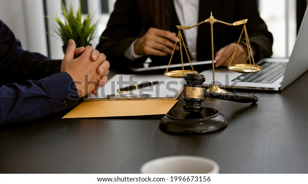 Lawyer discussing contract documents\
sitting at a desk at the office Legal concepts, advice, legal\
advisory services and scales with a judge\'s hammer put\
forward.