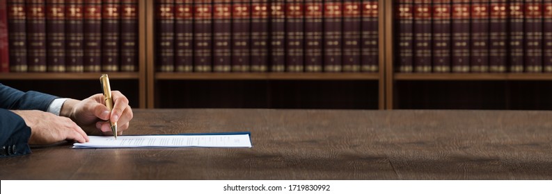 Lawyer Doing Legal Document Scrutiny At Desk With Books At Background 