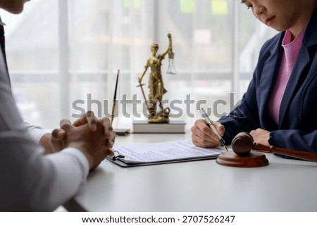 Lawyer is explaining contract details to client in office using pen and contract document, with gavel and Themis statue in background