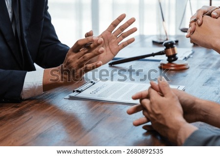 Lawyer explaining contract terms to client using persuasive hand gestures, with contract, gavel and scale on wooden table