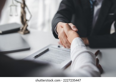 Lawyer shaking hands with a client making about documents, contracts, agreements, cooperation agreements with a female client at the lawyer's desk and a hammer at the table. - Shutterstock ID 2227235447