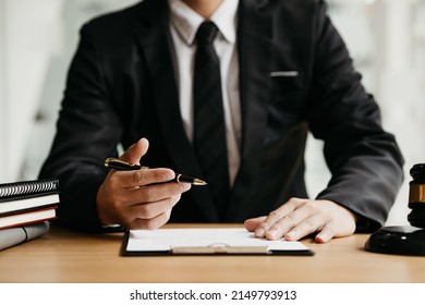 A lawyer sits in his office, on a table with a small hammer to beat the judges desk in court. and justice scales, lawyers are drafting a contract for the client to use with the defendant to sign.