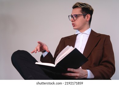 Lawyer sitting in front of a white background talking. Business man sitting with the black book on him. Teacher dressed in a suit presenting a topic. Elegant man dressed in jacket, shirt and glasses