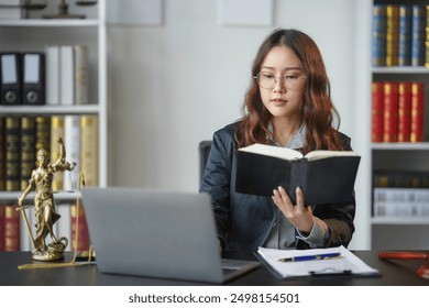 Lawyer is sitting at her desk reading a law book while working on a case in her office - Powered by Shutterstock