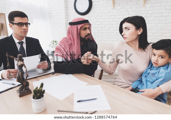 Lawyer in suit in office with\
arab husband and wife. Man is begging his wife, woman is holding\
son.
