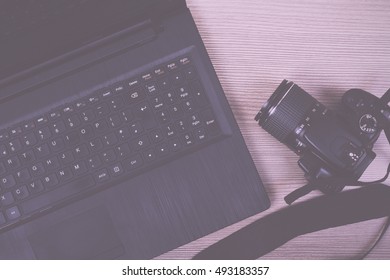 Lay flat image of a laptop and camera on a wooden surface Vintage Retro Filter.
