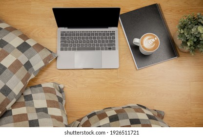 Lay flat view of working space with laptop, pillow, document and latte coffee on wooden floor in house shows concept of working from anyway by using digital networking via internet for modern life.