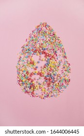 Lay out a flat composition of candy in the shape of an egg on a pink background. The view from the top.