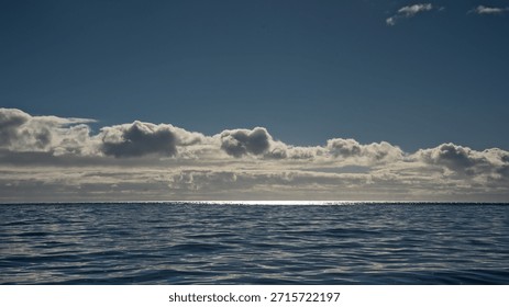 layer of cumulus clouds under a clear blue sky over the Atlantic ocean with bright sun reflections on the horizon