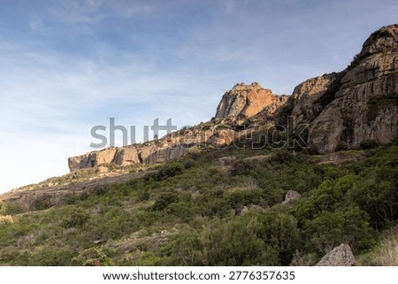 layered cliffs of Roquebrune Rock in Roquebrune-sur-Argens, Var, France, with rock formations, scrub vegetation and side sunlight. The scene has sunlight from the right side.