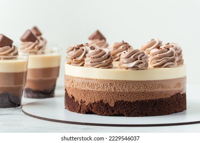 Layered dessert Trifles in a transparent glass.  Sponge biscuit and three chocolate mousse layers. Chocolate souffle trifle cake in individual disposable transparent cups. White background