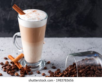 Layered latte coffee on the table in a tall glass. Roasted coffee beans, cinnamon sticks