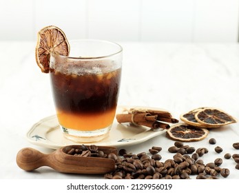Layered non-alcoholic cocktail recipe idea. Orange juice in the bottom and dark coffee on the top in the glass. Bright and cozy still life of coffee beans, orange slices and layered cocktail. - Shutterstock ID 2129956019