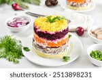 Layered salad with beet, herring, carrots and potatoes on white plate