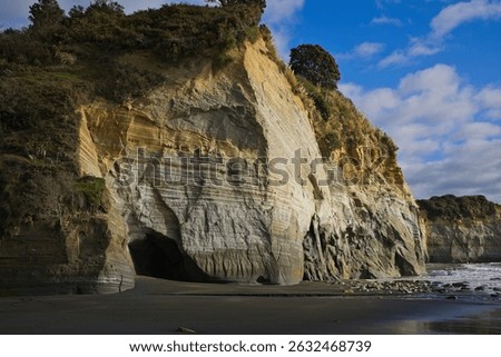 Layered white seaside cliffs rise from the ocean, streaked with striations of rust, beige, and grey. The textured rock face glows under soft light, revealing the coast’s natural formation history.