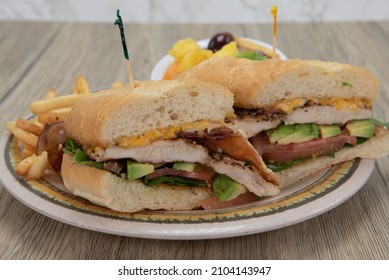 Layers Of Chicken, Bacon, And Avocado Slices Generously Built Into This Enormous Sandwich Sered With French Fries.