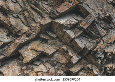 Layers and cracks in sedimentary rock on cliff face, background. Cliff of rock mountain. Rock slate in the mountain. Cracks and layers of sandstone.