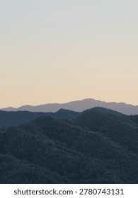 Layers of mountain ridges under a soft pastel sunset sky, beautiful minimalist mountain range landscape at dusk.