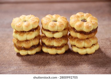 Layers of pineapple jam-filled biscuits are stacked on a brown wooden floor.