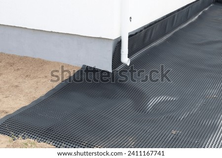 Laying a black waterproofing membrane around the foundation of a house. Construction of the blind area of the house. Reliable protection of the foundation from moisture. 