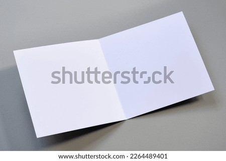 Laying blank empty square open greeting card mock up on clean cool grey background with copy space. For use as a Christmas, birthday, wedding or celebration background template.  