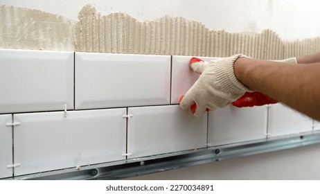 Laying ceramic tiles on the backsplash of the kitchen. A worker lays and installs white ceramic tiles in a kitchen. Ceramic tile-fish.