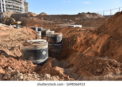 Laying Concrete Manholes And Heating Drain Pipes And For Stormwater System In Trench At Construction Site. Sewerage Manhole And Pipes Line Under Construction.  Chambers And Pump Station