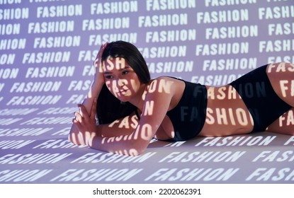 Laying Down On The Floor. Beautiful Young Woman Is In Projector Neon Lights In The Studio.