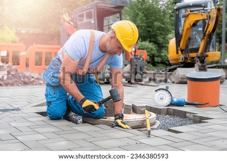 Laying interlocking paving. A worker is placing interlocking paving stones around the sewer manhole cover.