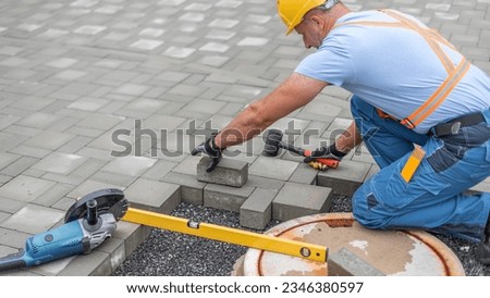 Laying interlocking paving. A worker is placing interlocking paving stones around the sewer manhole cover.